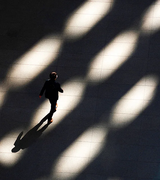 A person seen from above, walking across a sunlit floor between long diagonal shadows