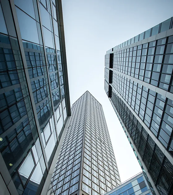 Glass office towers seen from street level, rising into a bright sky