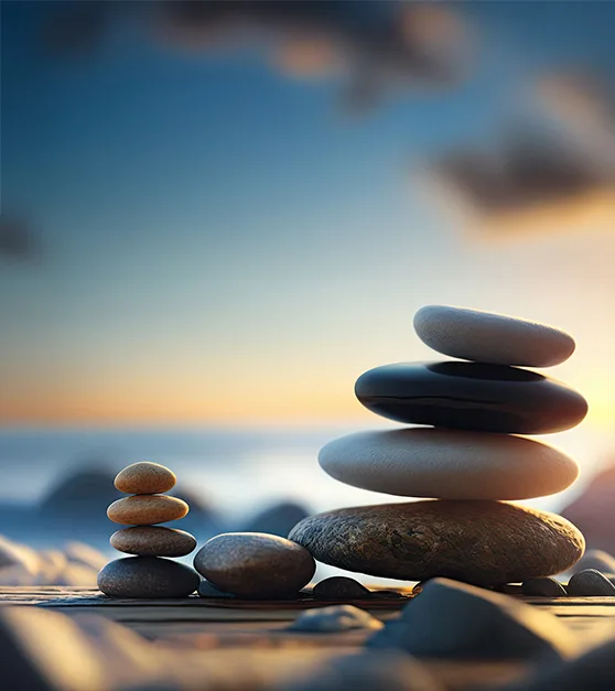 Stacked balancing stones on a wooden surface by the sea at sunset